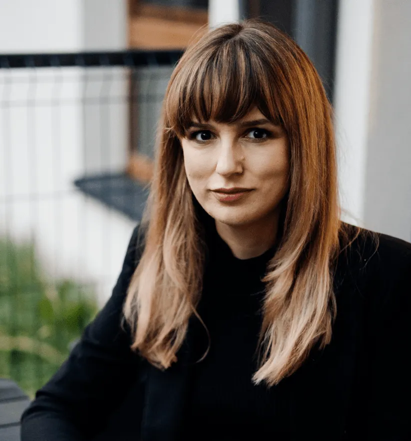 Kobieta siedząca przy stole, patrząca w kamerę, pracująca na laptopie
